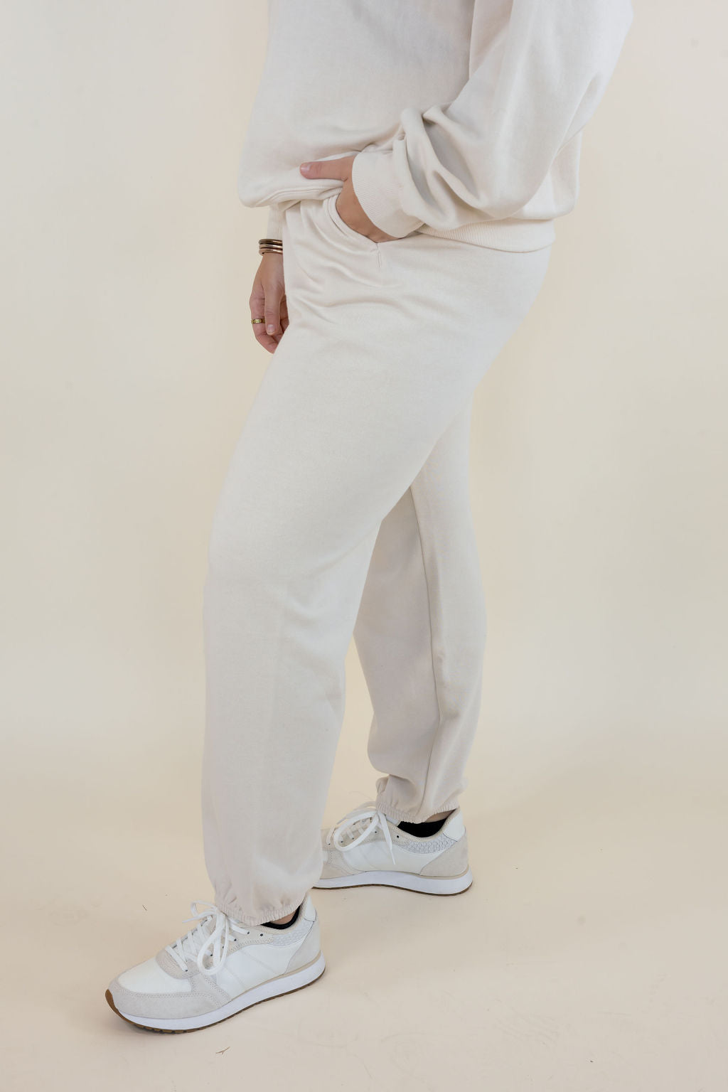 Side view of Frosted Pearl Uptown Classic Fleece Joggers showing relaxed leg fit, side seam pocket, and elastic ankle cuffs with white sneakers.