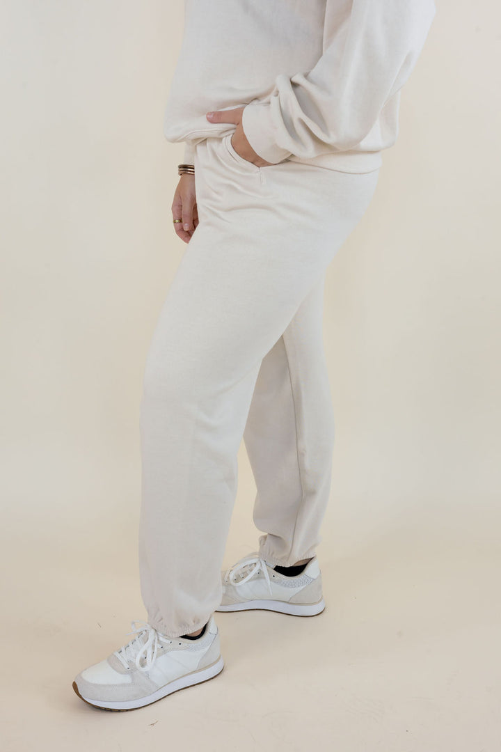 Side view of Frosted Pearl Uptown Classic Fleece Joggers showing relaxed leg fit, side seam pocket, and elastic ankle cuffs with white sneakers.