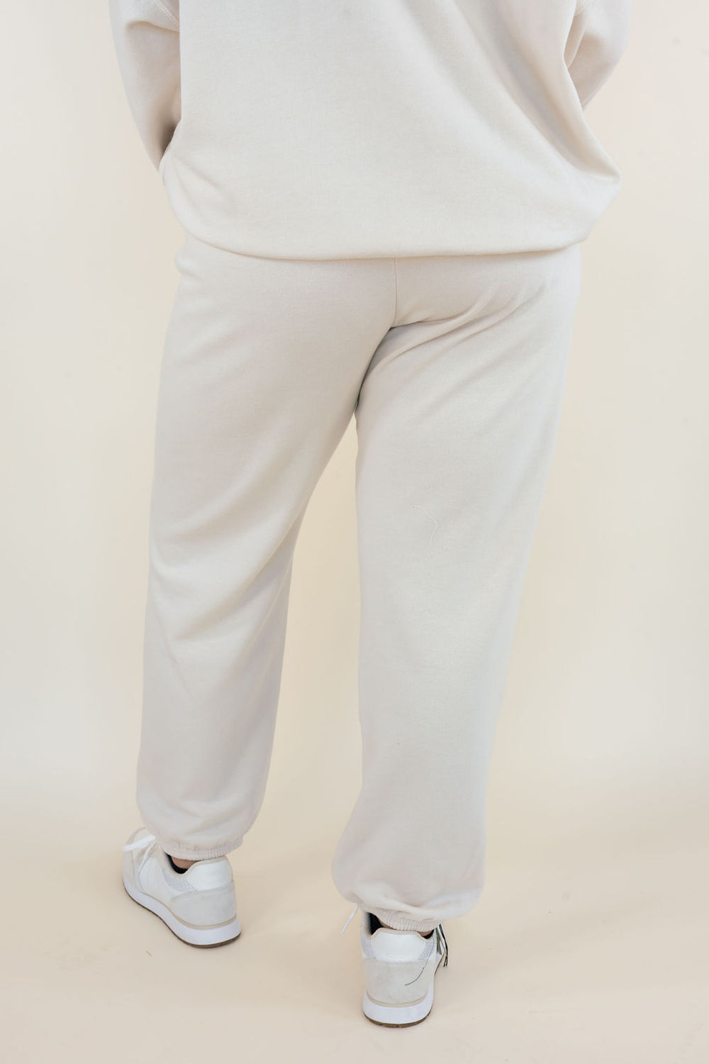 Back view of Uptown Classic Fleece Joggers in Frosted Pearl showing relaxed fit through the legs, elastic ankle cuffs, and soft cream-colored fleece fabric.