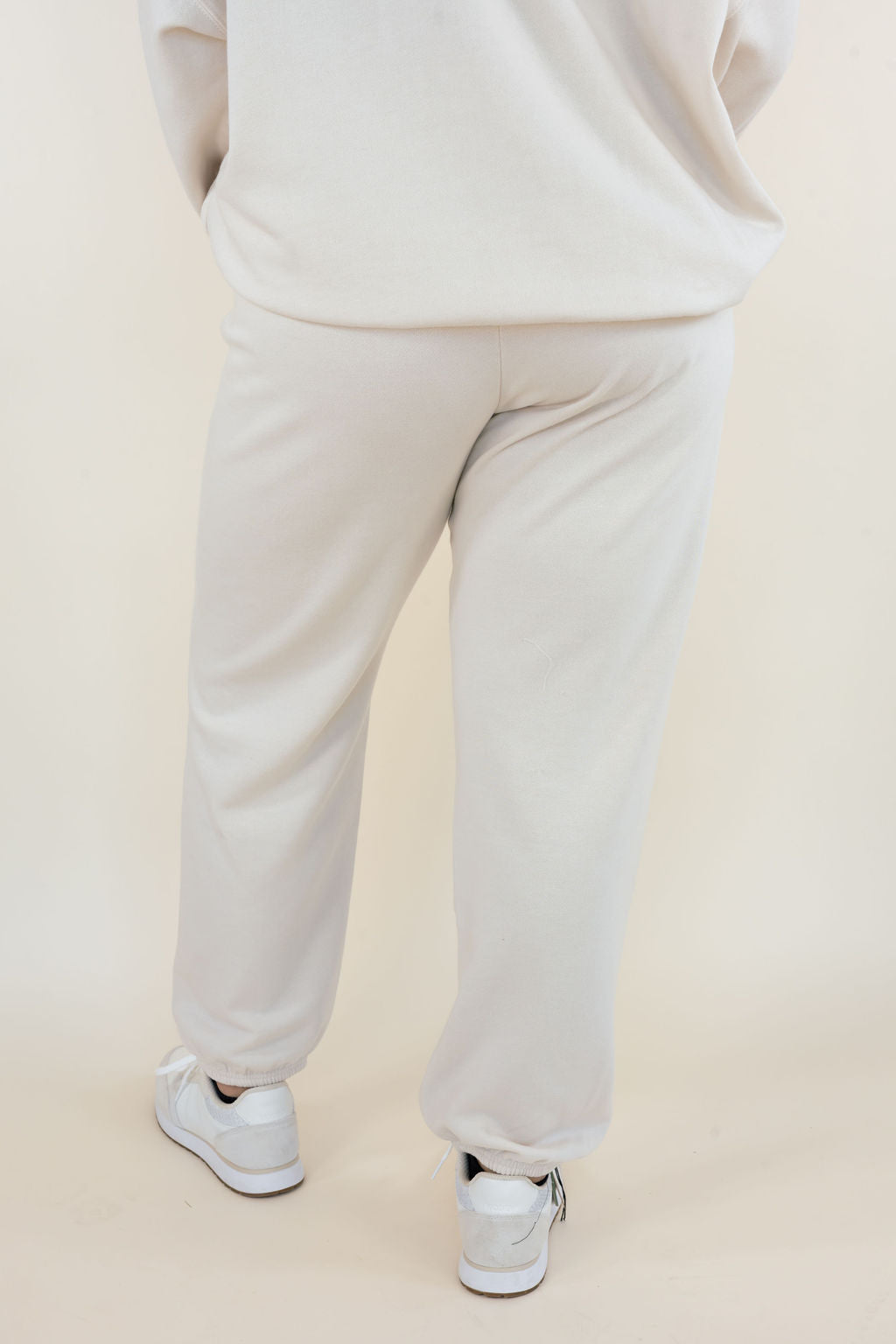Back view of Uptown Classic Fleece Joggers in Frosted Pearl showing relaxed fit through the legs, elastic ankle cuffs, and soft cream-colored fleece fabric.