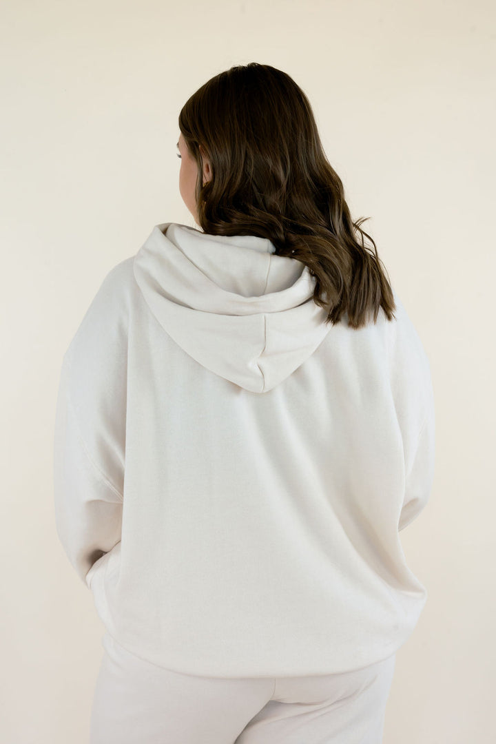 Close-up back view of Frosted Pearl First Quarter Hoodie featuring a roomy hood, dropped shoulders, and soft cream-colored fleece fabric.