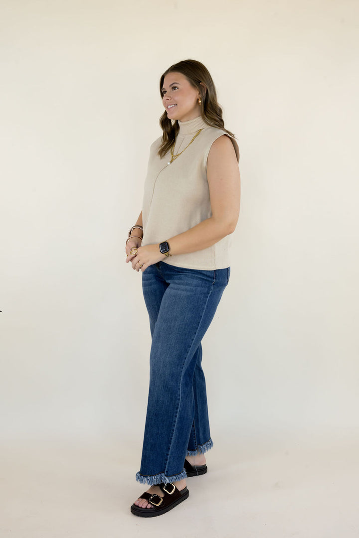 Side view of woman wearing cream sleeveless mock neck knit top showing the relaxed silhouette, high neckline, and hip-length hem