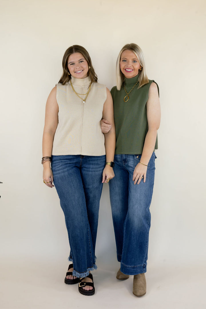Two women modeling sleeveless mock neck knit tops in cream and olive green featuring relaxed silhouettes, high necklines, and blue wide leg jeans