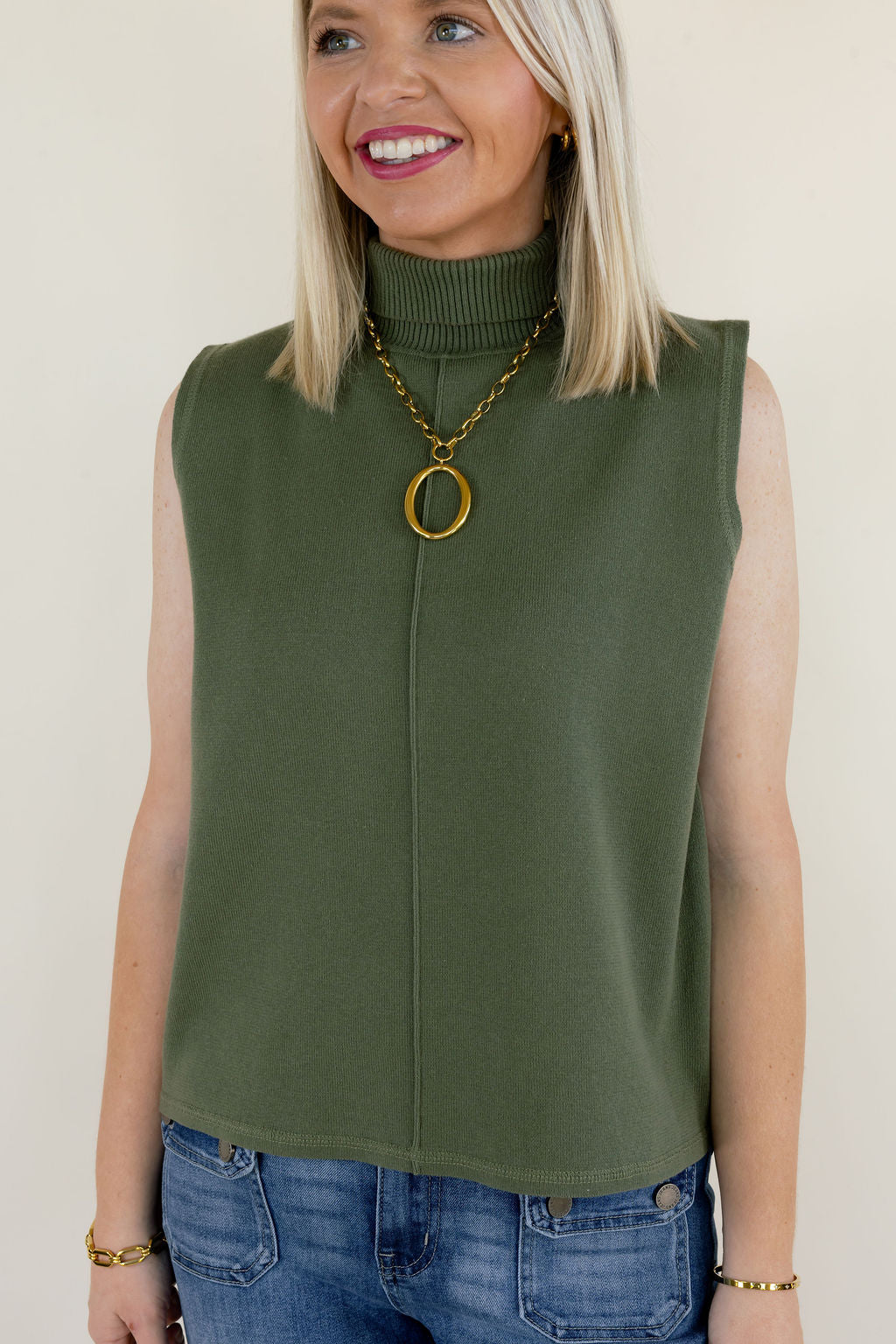 Close-up of olive green sleeveless mock neck sweater top featuring a high neckline, subtle front seam detail, and relaxed fit