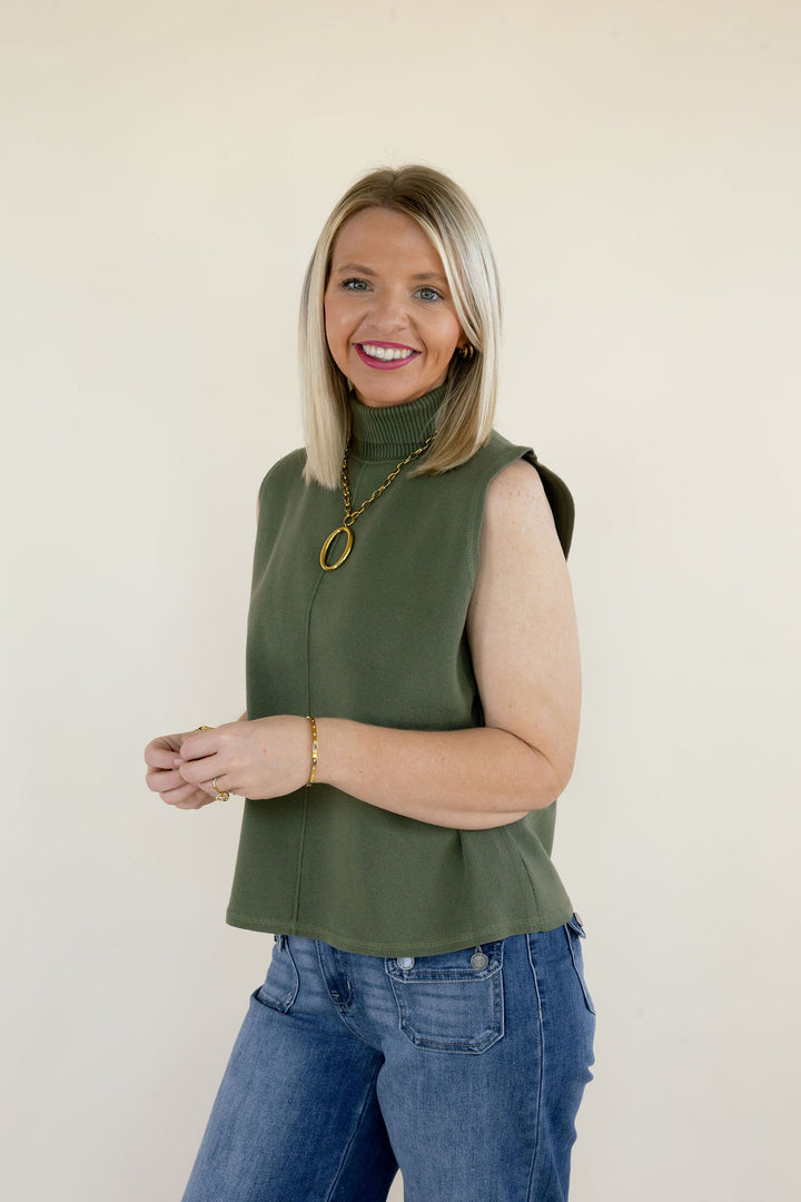 Three-quarter view of olive green sleeveless mock neck knit top showing the high neckline, relaxed silhouette, and gold statement necklace