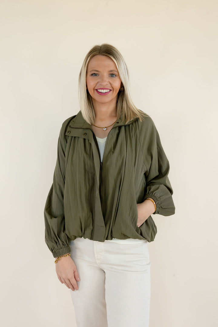 Front view of woman modeling olive green collared blouse featuring long balloon sleeves, gathered neckline, and relaxed fit styled with white pants