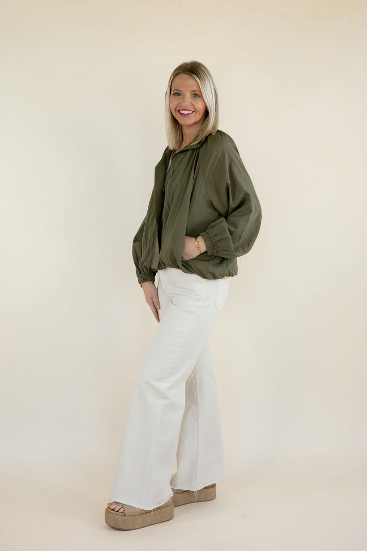 Side view of woman wearing olive green collared blouse with voluminous sleeves, relaxed silhouette, and white wide leg pants
