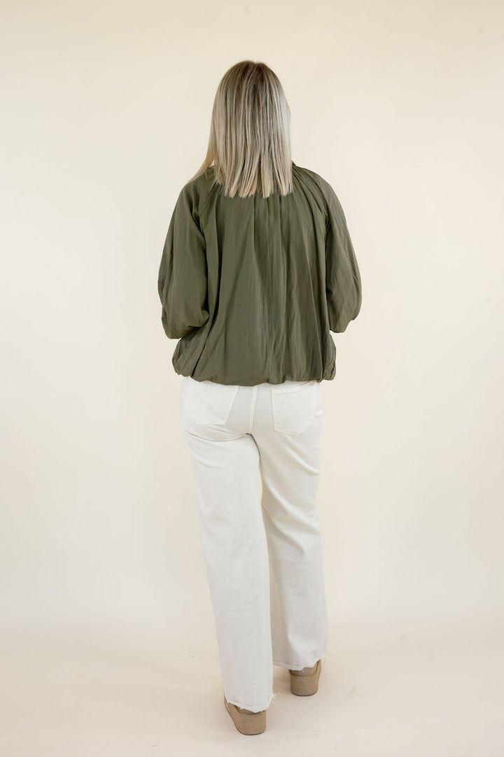 Full back view of woman wearing olive green collared blouse with white pants, highlighting the loose fit and gathered back yoke