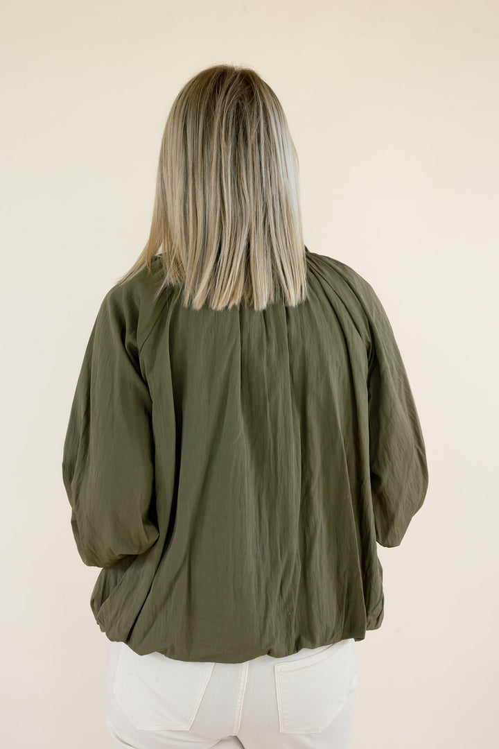 Close-up back view of olive green collared blouse showing gathered fabric across the upper back, voluminous sleeves, and relaxed hem