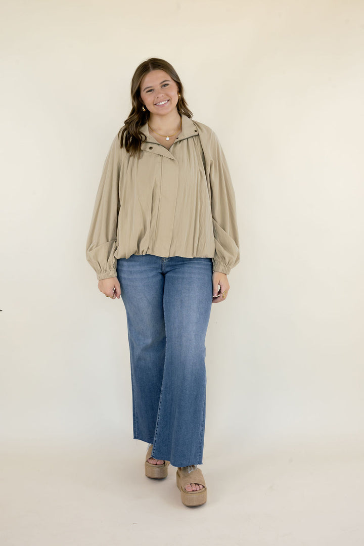 Woman modeling beige collared long sleeve blouse with gathered neckline, voluminous balloon sleeves, relaxed fit, and blue wide leg jeans