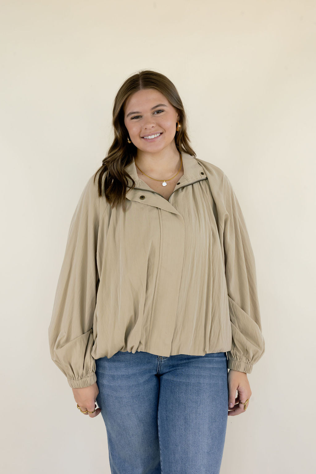 Woman wearing beige collared long sleeve blouse with gathered fabric detailing, relaxed silhouette, and blue jeans