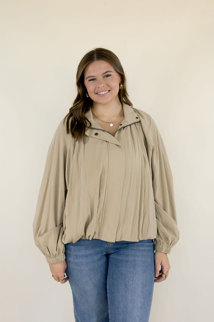 Woman wearing beige collared long sleeve blouse with gathered fabric detailing, relaxed silhouette, and blue jeans