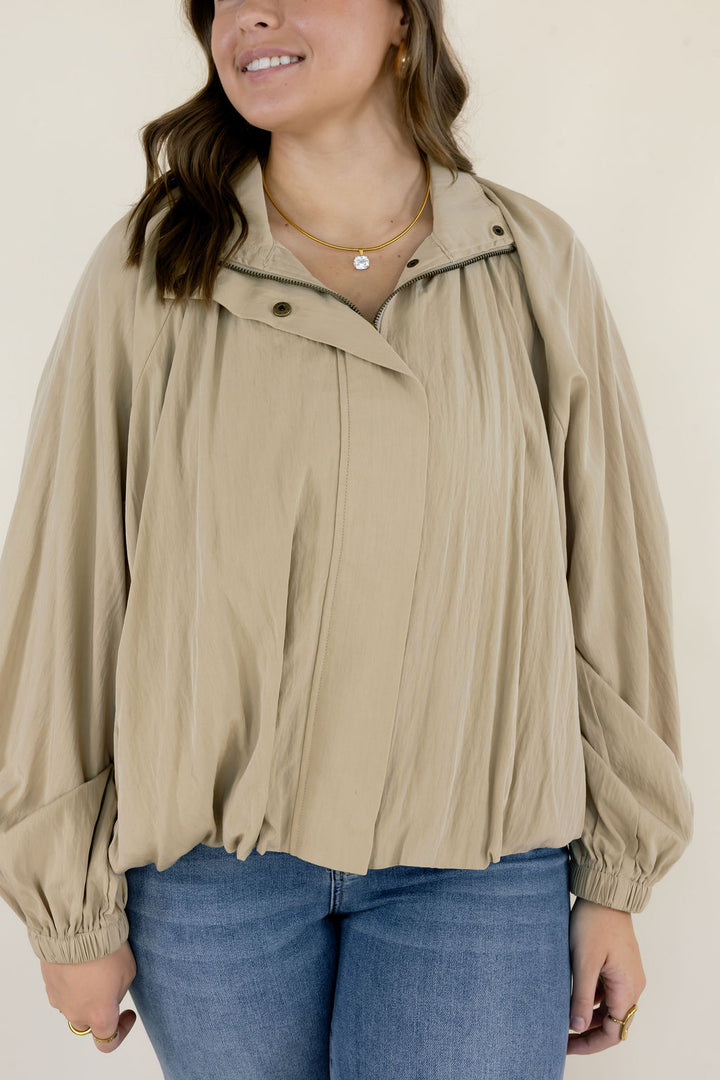 Close-up of beige collared blouse showing the gathered neckline, button details, voluminous long sleeves, and softly gathered hem