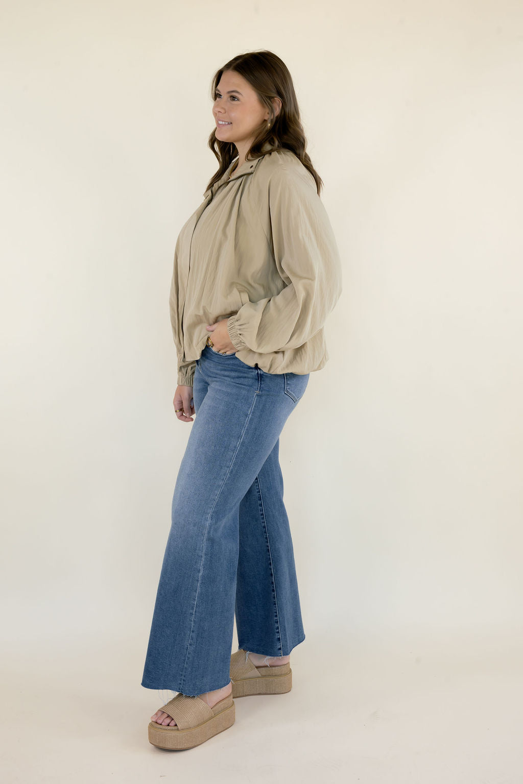 Side view of beige collared blouse showing gathered neckline, balloon sleeves, and relaxed fit styled with blue wide leg jeans