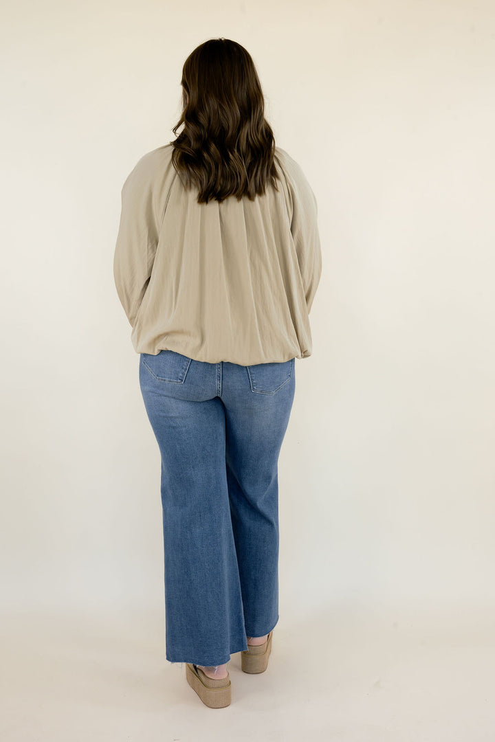 Full back view of woman wearing beige collared blouse with blue wide leg jeans, showing the relaxed silhouette and gathered back detailing