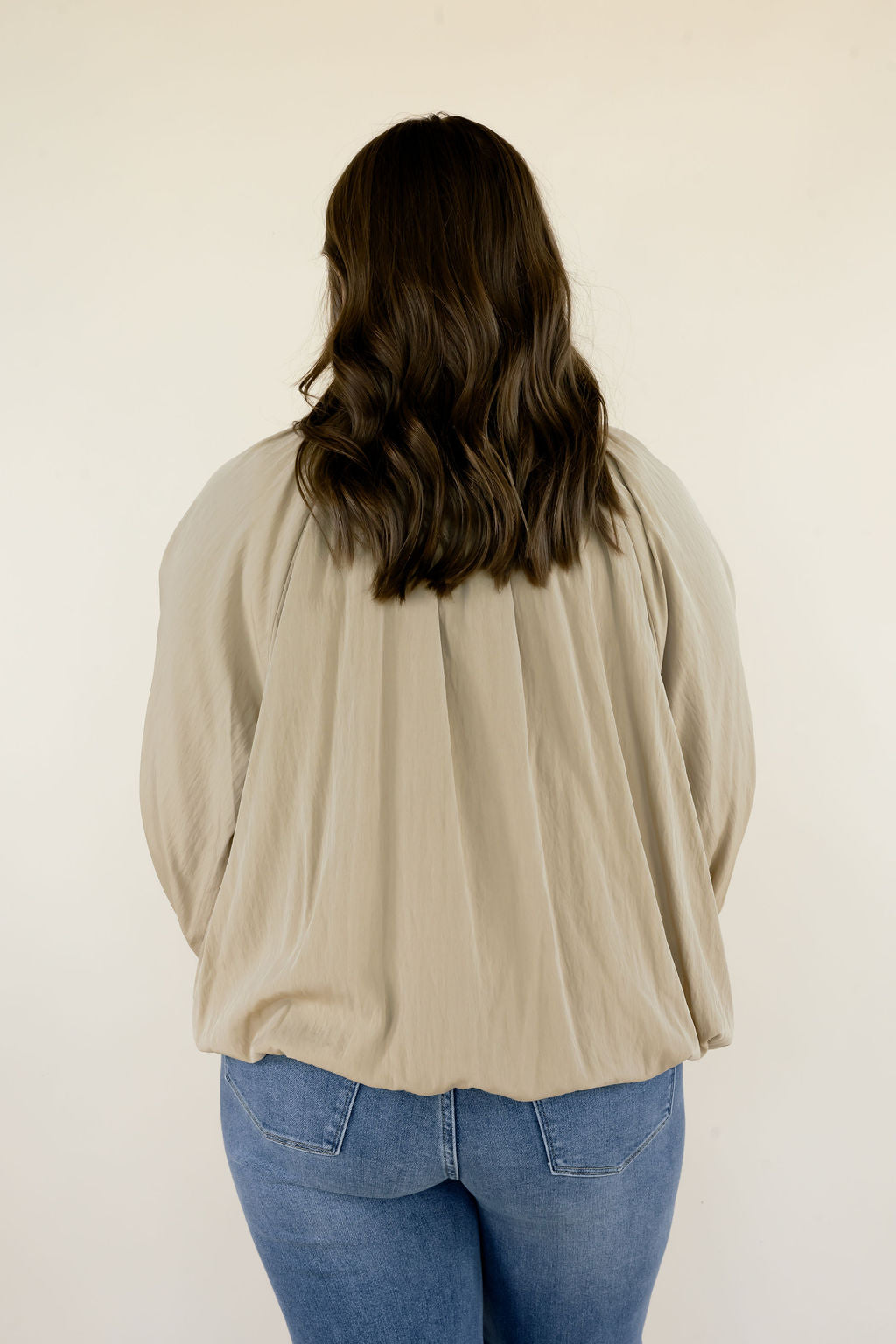 Close-up back view of beige collared blouse showing gathered back detailing, loose silhouette, and long sleeves