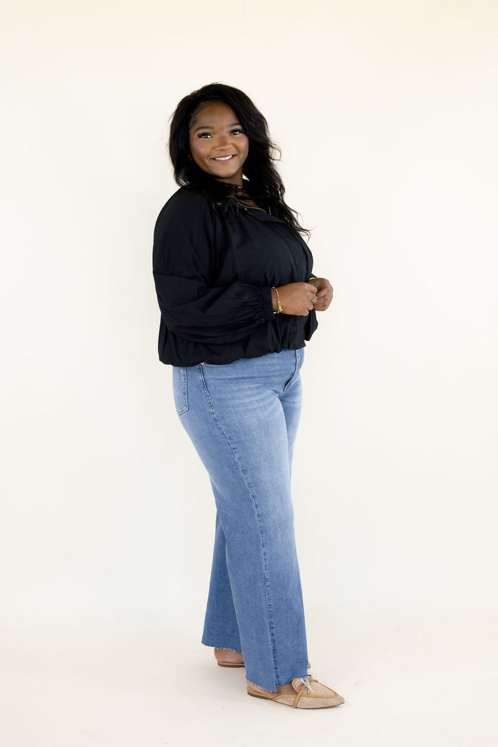 Side view of woman modeling black collared balloon sleeve blouse with light wash wide leg jeans and neutral flats