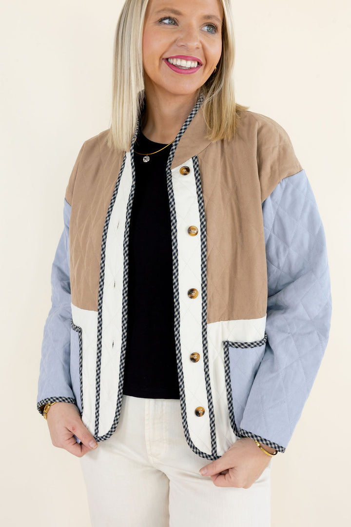 Close-up of colorblock quilted jacket highlighting the camel brown quilted upper panel, ivory button placket, light blue sleeves, and decorative contrast trim