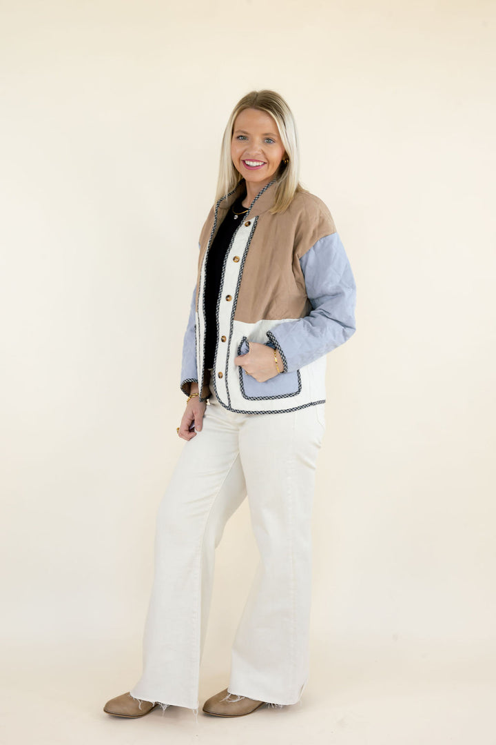 Side view of woman modeling camel brown and light blue colorblock quilted jacket with front patch pockets, ivory panels, and white wide leg pants