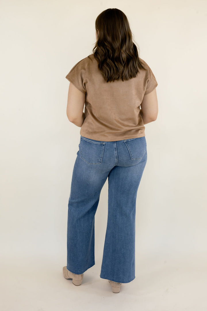 Back view of brown faux suede short sleeve top with a relaxed silhouette and hip-length hem, paired with blue wide-leg denim jeans.