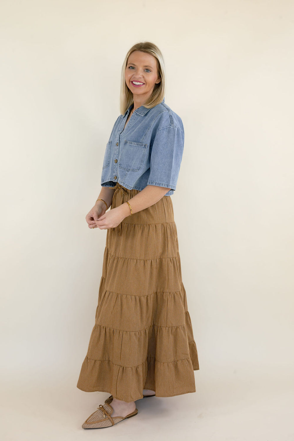 Side view of women's light wash cropped denim shirt with short sleeves, button-front closure, and relaxed silhouette, paired with a camel brown flowy maxi skirt.