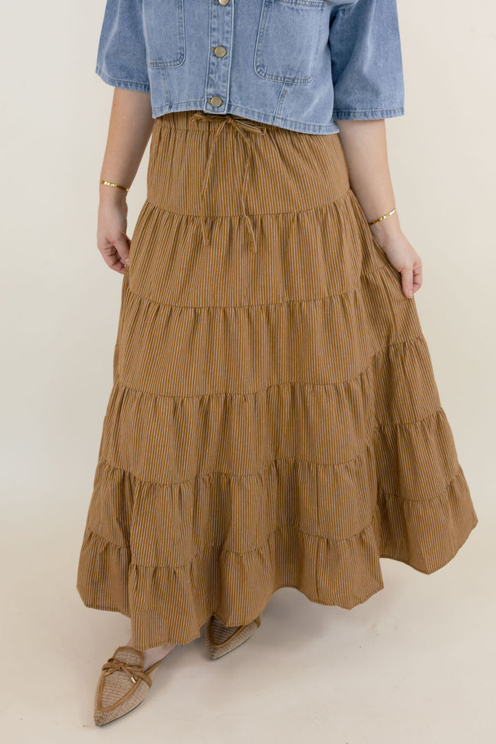 Camel brown boho maxi skirt featuring a stretchy elastic waistband, tiered ruffle detailing, and flowy lightweight silhouette styled with a denim top.