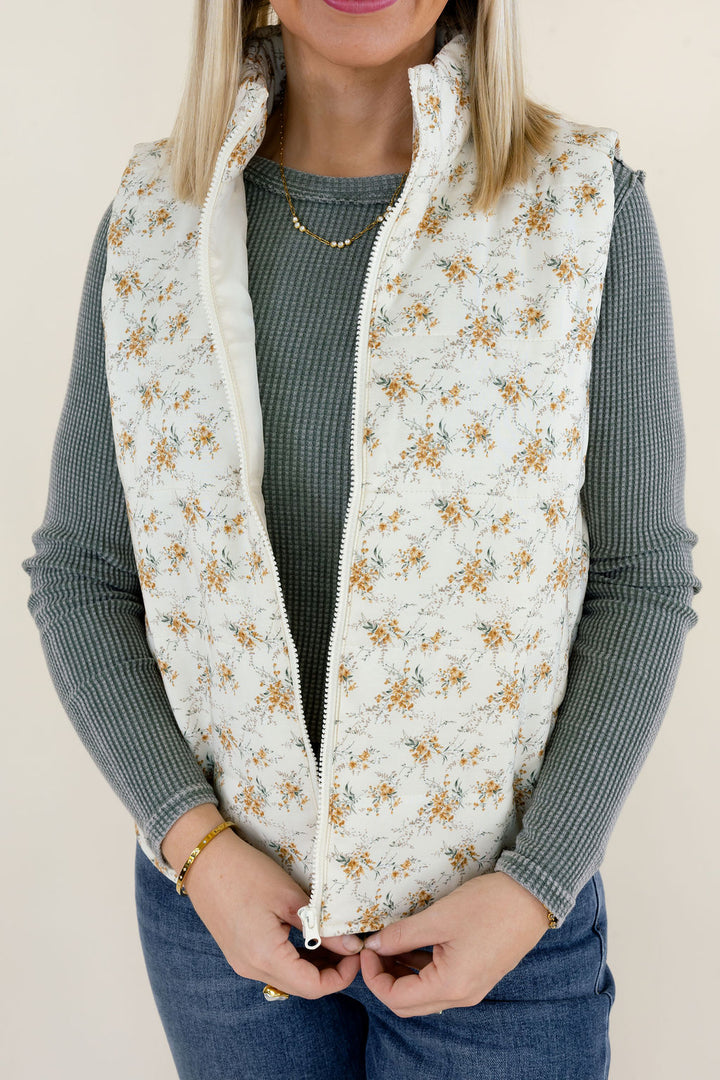 Close-up of ivory floral quilted vest highlighting the small golden botanical pattern, front zipper, quilted texture, and stand collar
