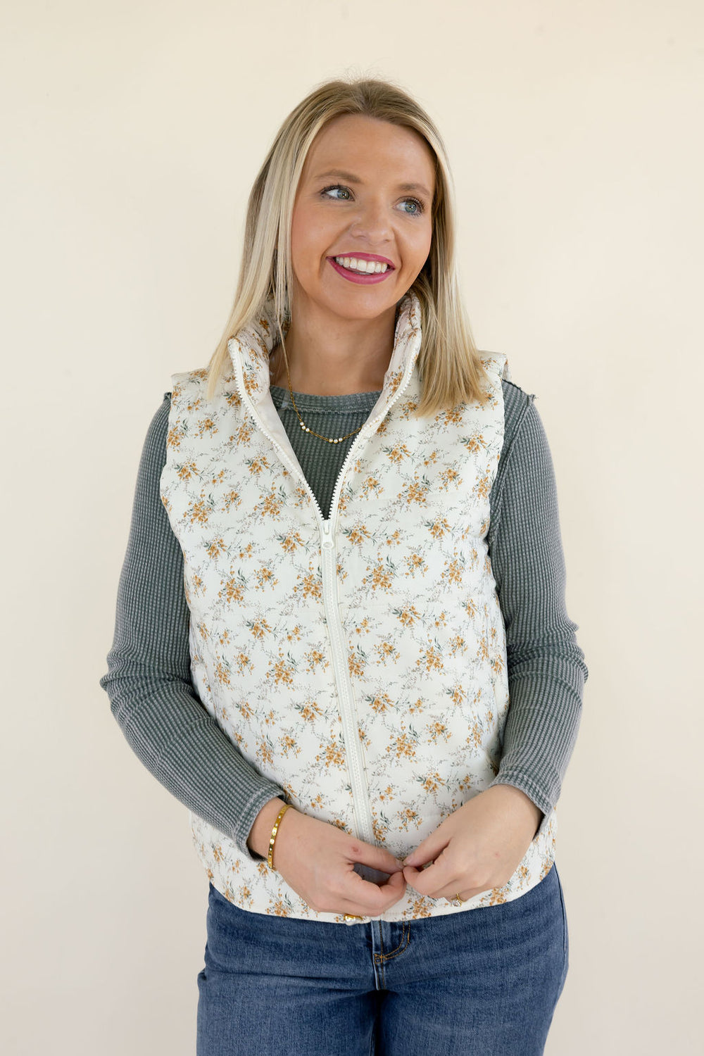 Front view of ivory floral quilted puffer vest featuring delicate golden floral print, stand collar, sleeveless design, and zip-up closure