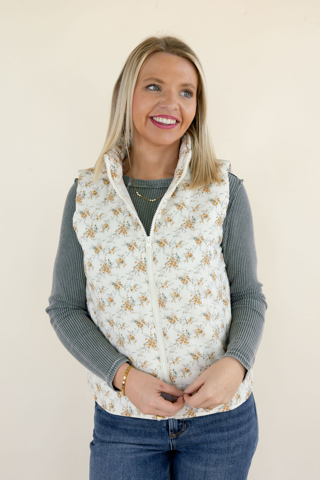 Front view of ivory floral quilted puffer vest featuring delicate golden floral print, stand collar, sleeveless design, and zip-up closure