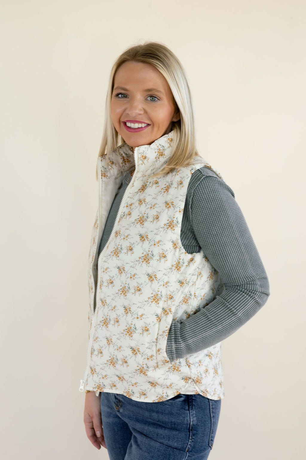 Three-quarter side view of ivory floral quilted vest highlighting the sleeveless armholes, quilted fabric, high collar, and side pockets