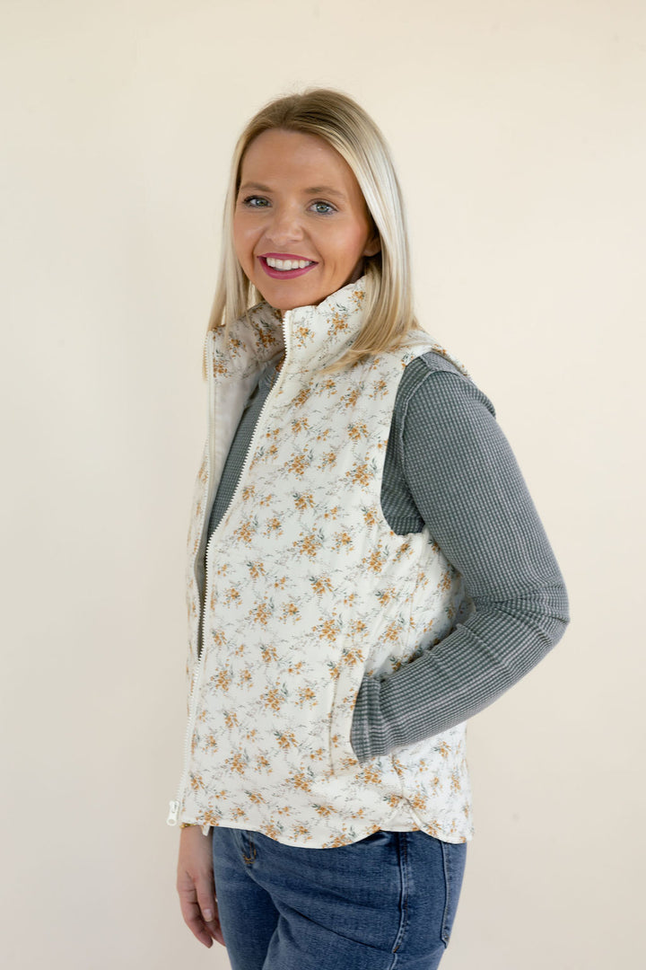 Three-quarter side view of ivory floral quilted vest highlighting the sleeveless armholes, quilted fabric, high collar, and side pockets