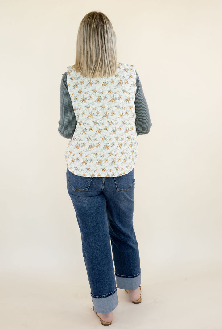 Back view of woman wearing ivory floral quilted vest showing the allover golden floral print, sleeveless silhouette, and hip-length hem