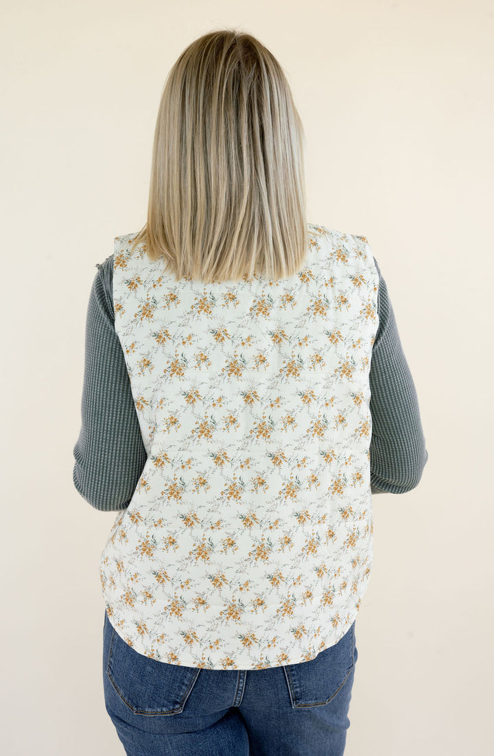 Close-up back view of ivory floral quilted vest highlighting the delicate golden botanical pattern, quilted texture, stand collar, and straight hem