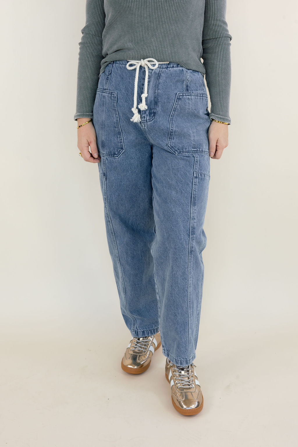 Front view of light wash denim cargo pants showing adjustable white drawstring waist, large front patch pockets, relaxed fit, and full-length legs