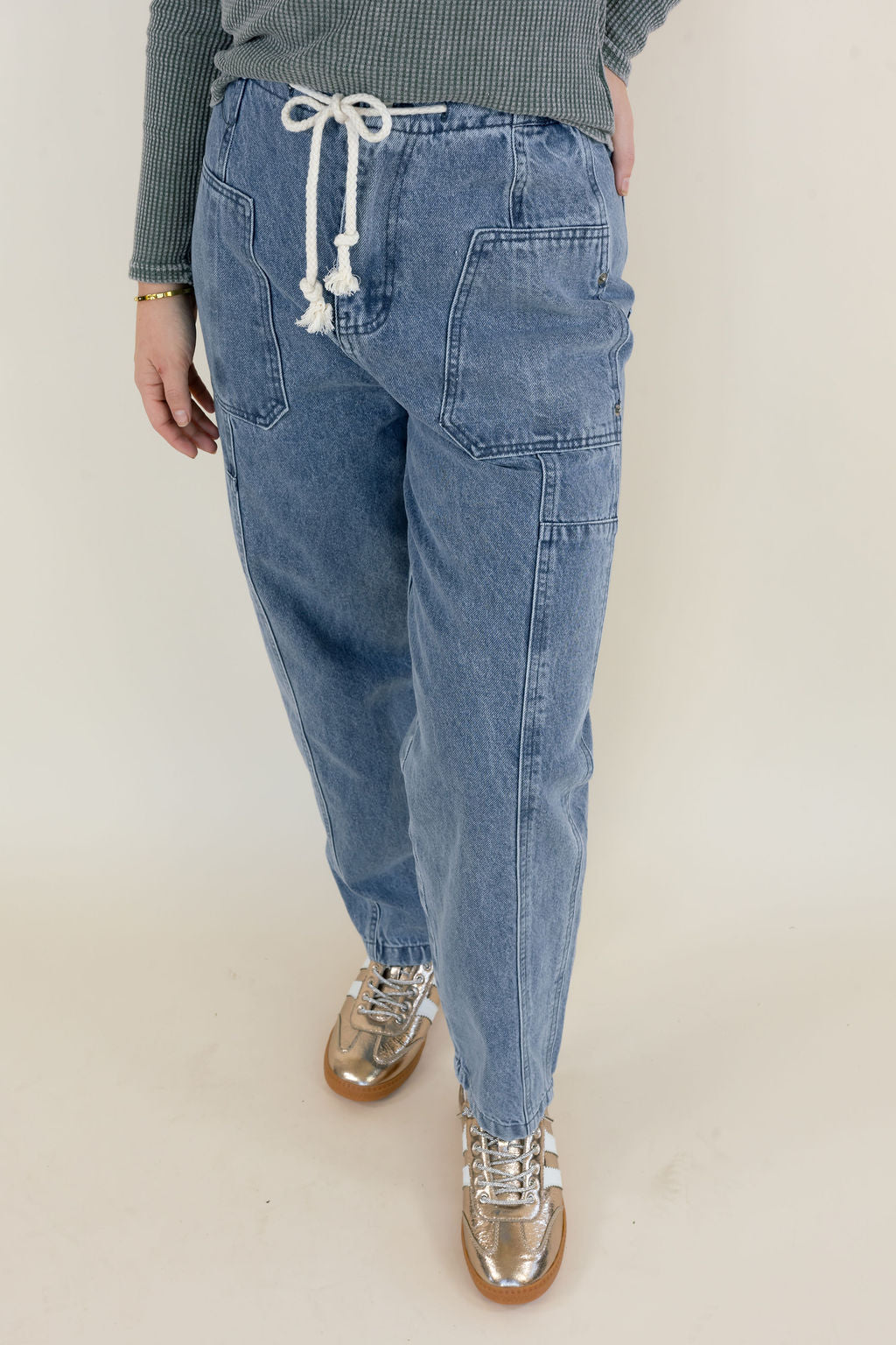 Front view of light wash denim cargo pants featuring large patch pockets, adjustable drawstring waist, straight-leg fit, and raw hem detailing