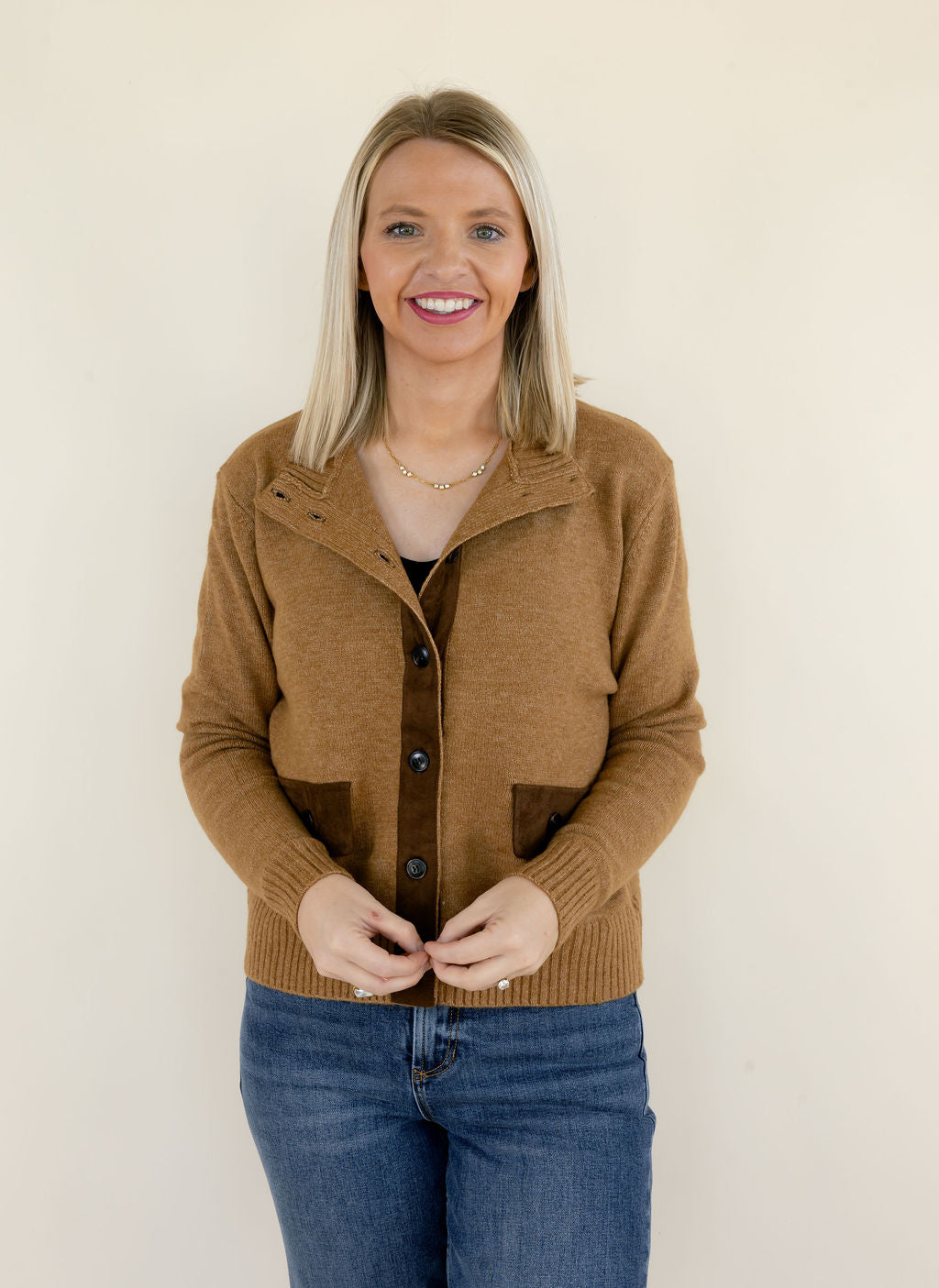 Woman modeling camel brown collared knit cardigan with dark brown buttons, contrasting patch pockets, ribbed cuffs, and blue jeans