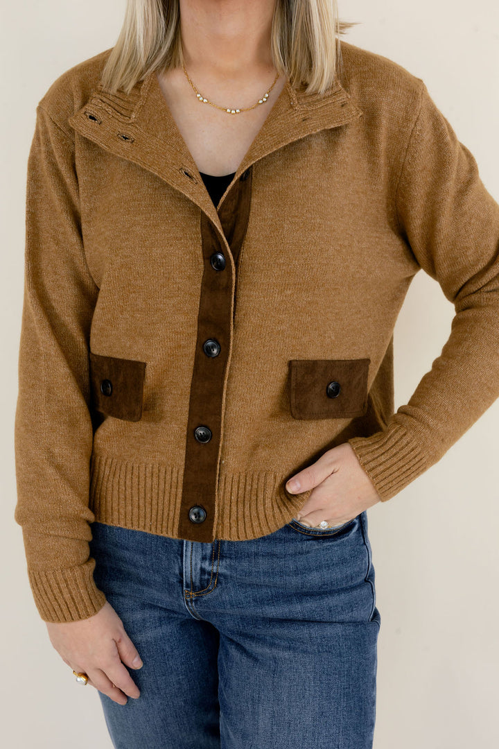 Close-up of camel brown knit cardigan highlighting the collared neckline, dark button closures, contrasting brown patch pockets, and ribbed hem