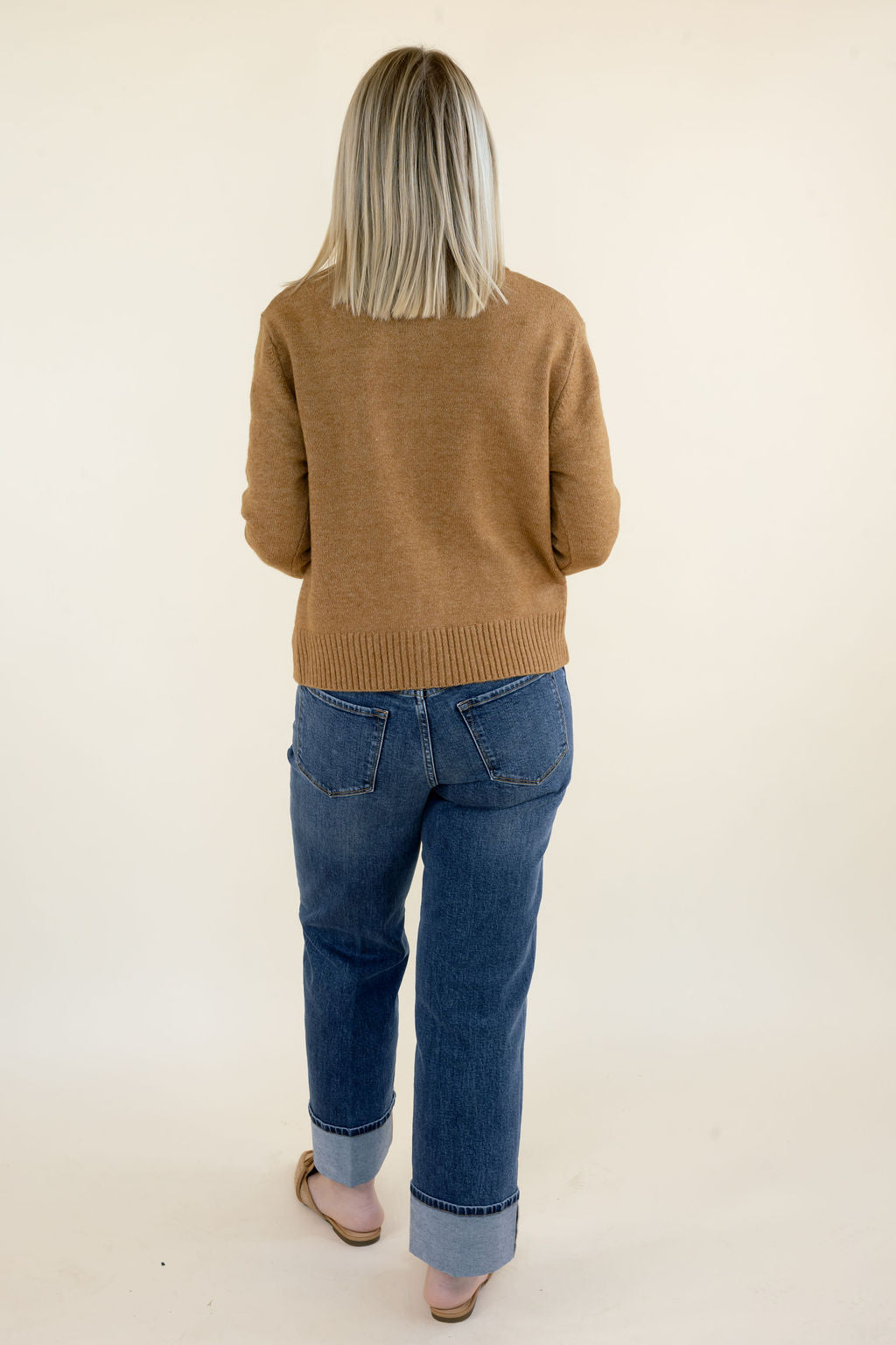 Back view of woman wearing camel brown knit cardigan with long sleeves, ribbed hem, and blue straight leg jeans