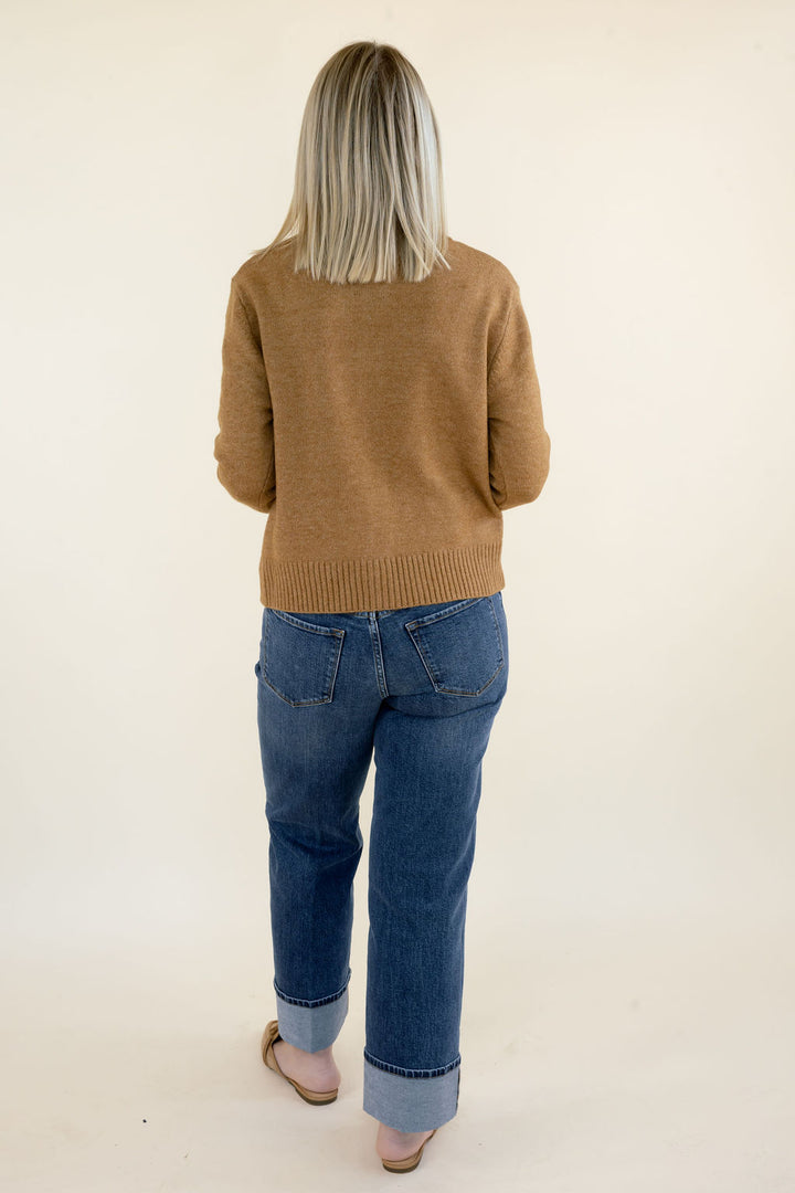 Back view of woman wearing camel brown knit cardigan with long sleeves, ribbed hem, and blue straight leg jeans
