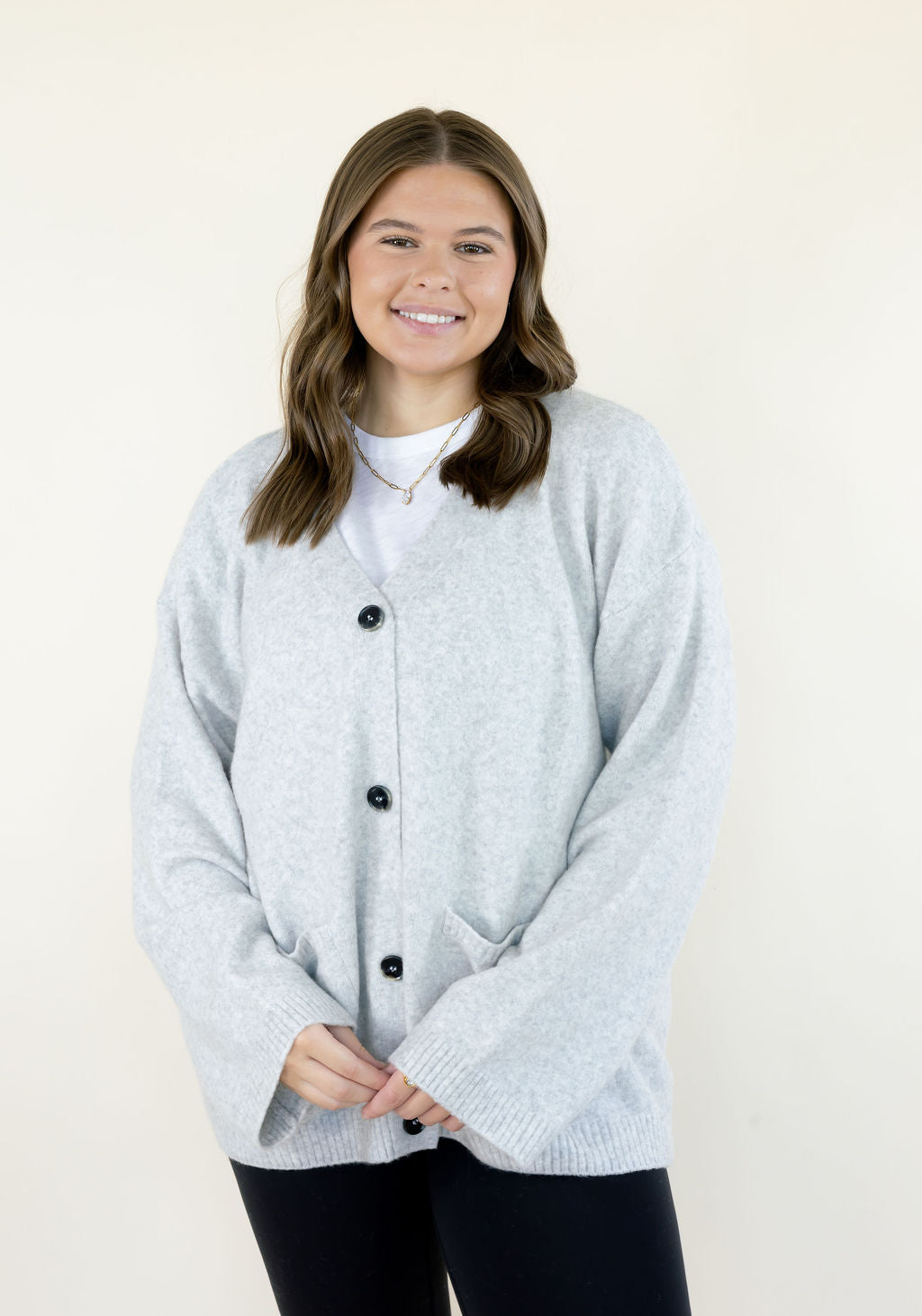 Women's light gray button-down cardigan sweater featuring a crew neckline, black buttons, long sleeves, and front pockets, styled with black leggings at Square 1 Boutique.