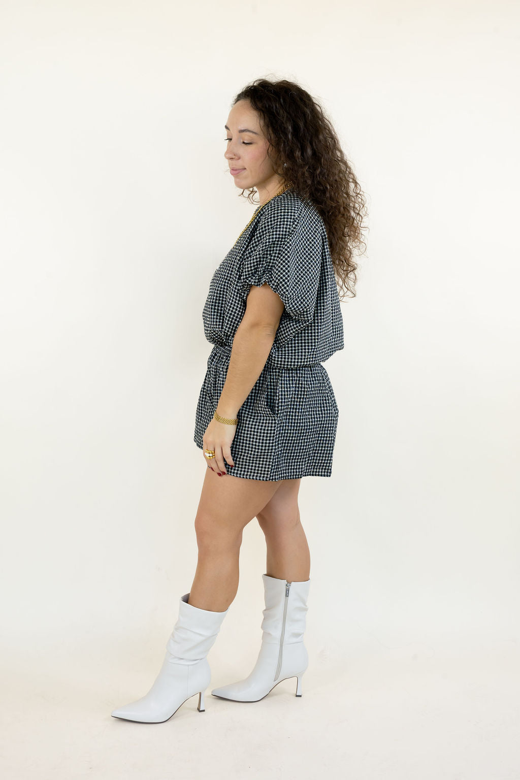 Side view of model wearing a black and white gingham two-piece shorts outfit with a relaxed short sleeve top, matching shorts, and white western boots.