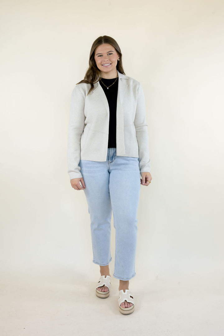 ivory button-down sweater jacket featuring a collared neckline and relaxed fit, paired with a black top and light wash straight leg jeans.