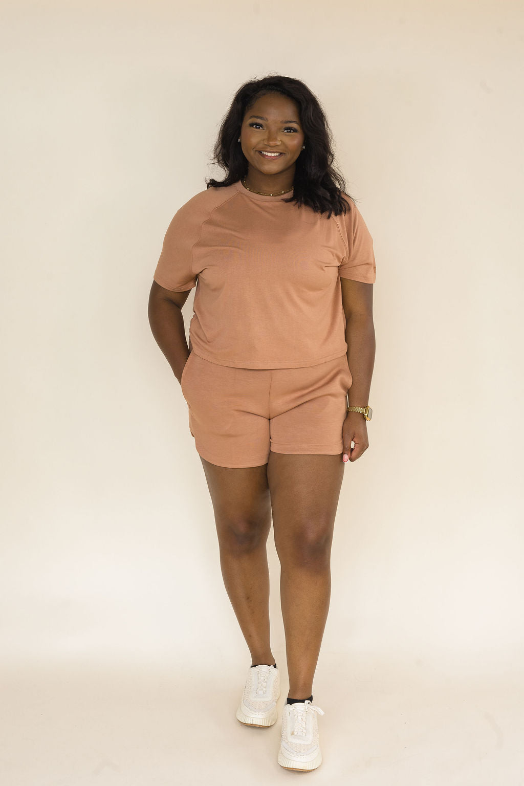 Woman wearing a mocha two-piece lounge set featuring a relaxed short sleeve crew neck top and matching pull-on shorts with side pockets styled with white sneakers.