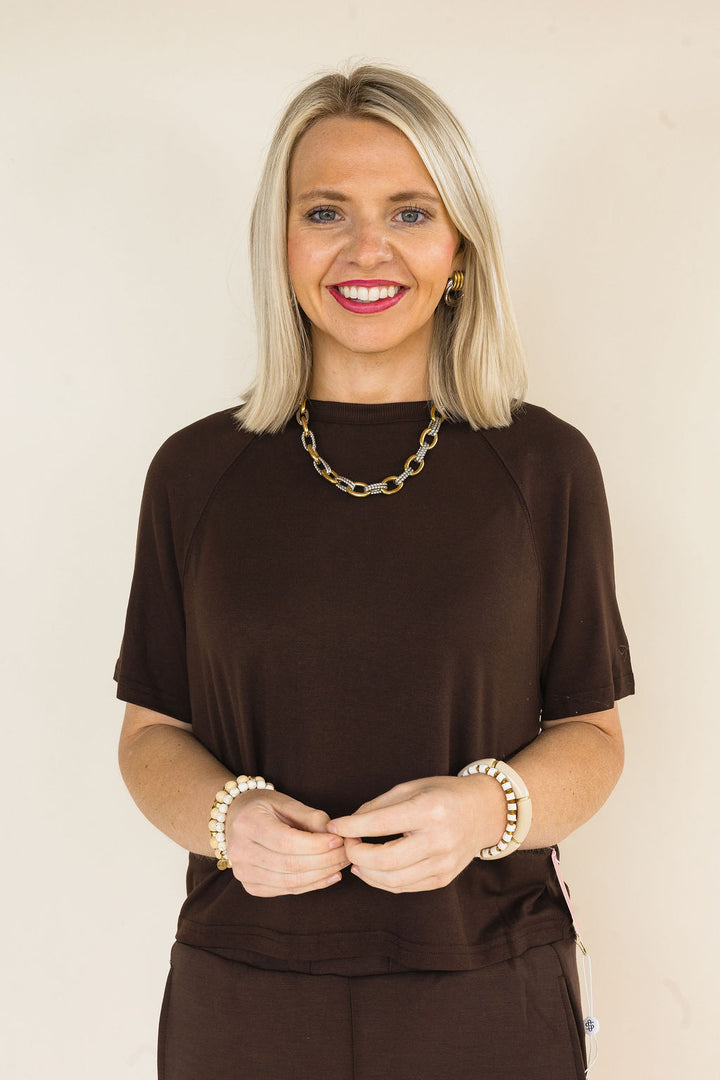 Close-up of a woman wearing a coffee brown two-piece lounge set featuring a relaxed short sleeve crew neck top and matching knit shorts with a soft, comfortable fit.