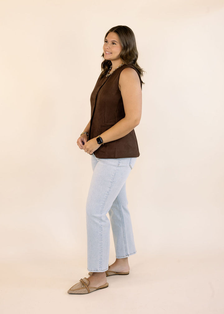 Woman modeling a brown sleeveless vest with light wash cropped jeans and woven pointed-toe flats on a neutral studio background.