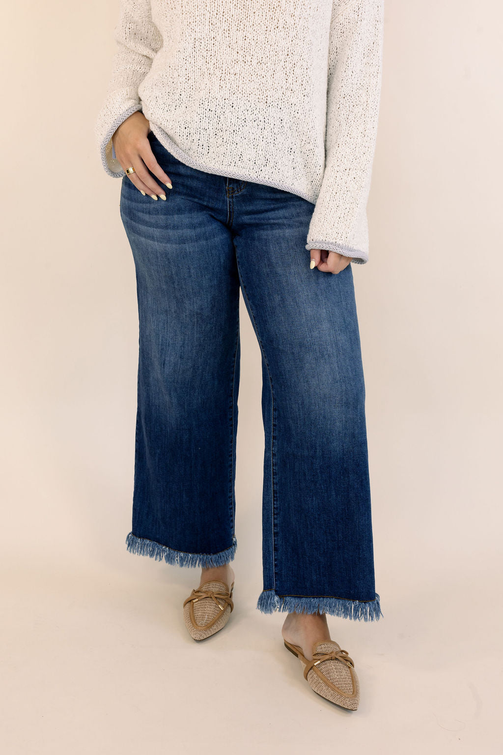 Dark wash wide leg jeans with raw fringe hem styled with a white knit sweater and woven pointed-toe flats.