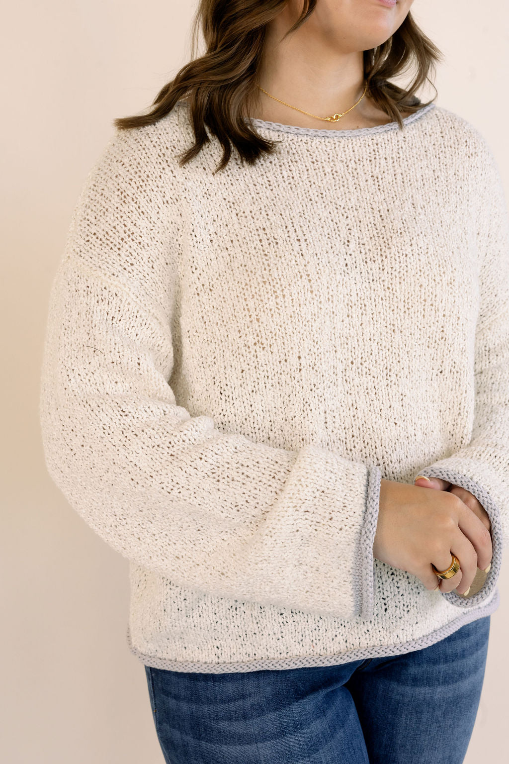 A woman wearing an oatmeal-colored, textured knit sweater with blue jeans, shown from the neck down against a plain beige background.