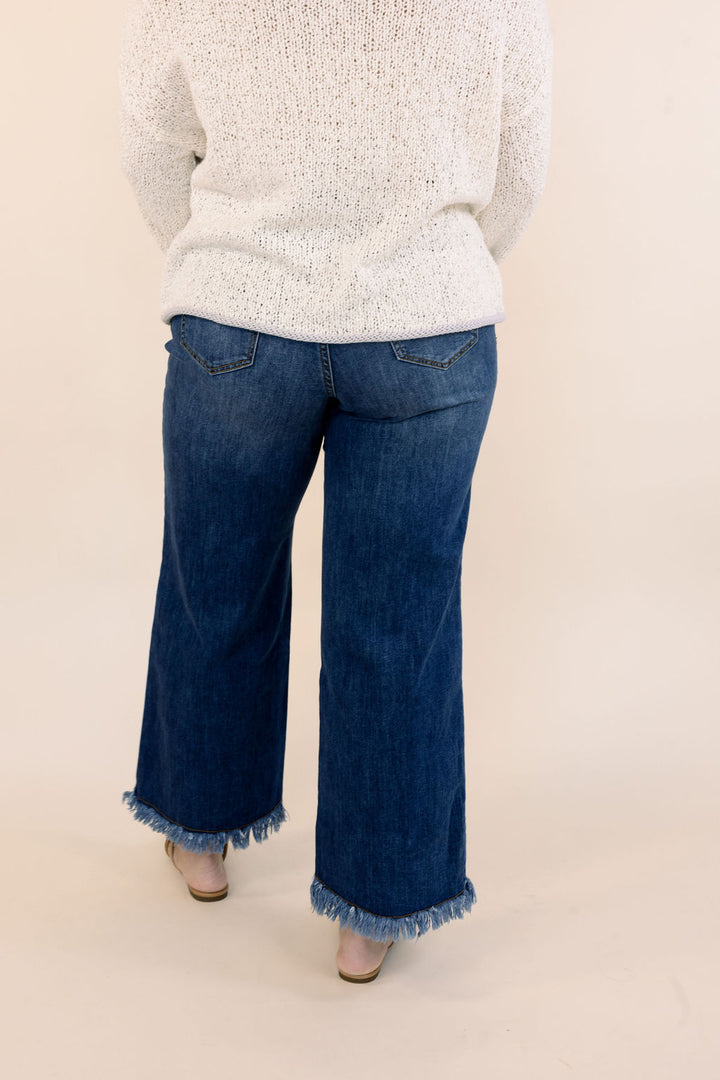Back view of dark wash wide leg jeans featuring back pockets and raw fringe hems.