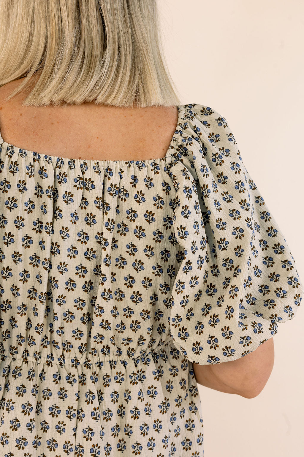 Close-up of a person wearing a cream-colored puff-sleeve top with a small blue and brown floral print, viewed from the back.