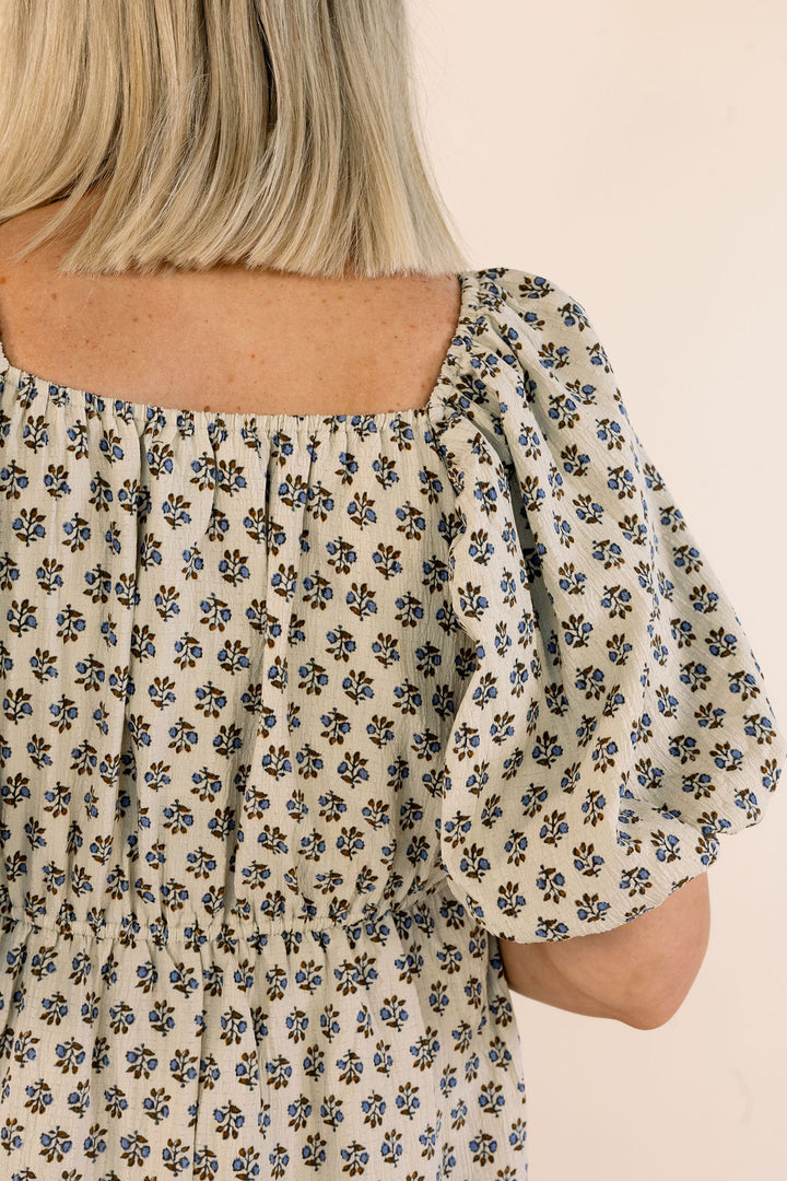 Close-up of a person wearing a cream-colored puff-sleeve top with a small blue and brown floral print, viewed from the back.
